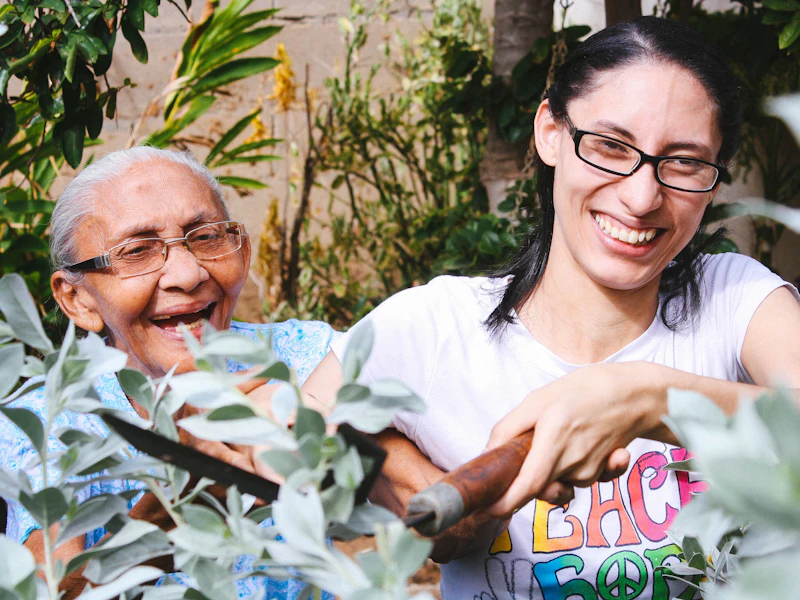 An older woman and a younger woman laughing together while gardening