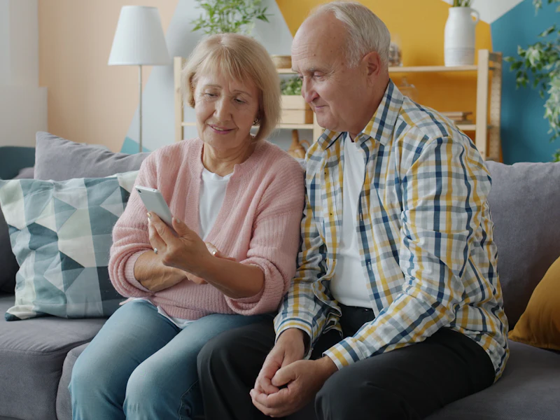 An older couple sitting on their sofa at home, looking at a phone together